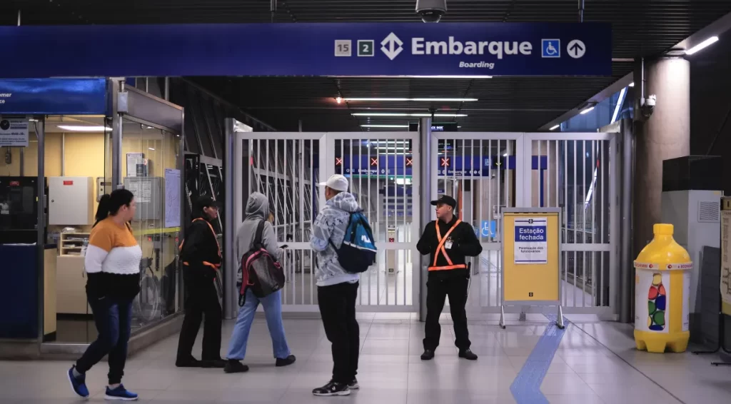 Foto de uma entrada do metrô fechado com pessoas circulando e segurança guardando a entrada